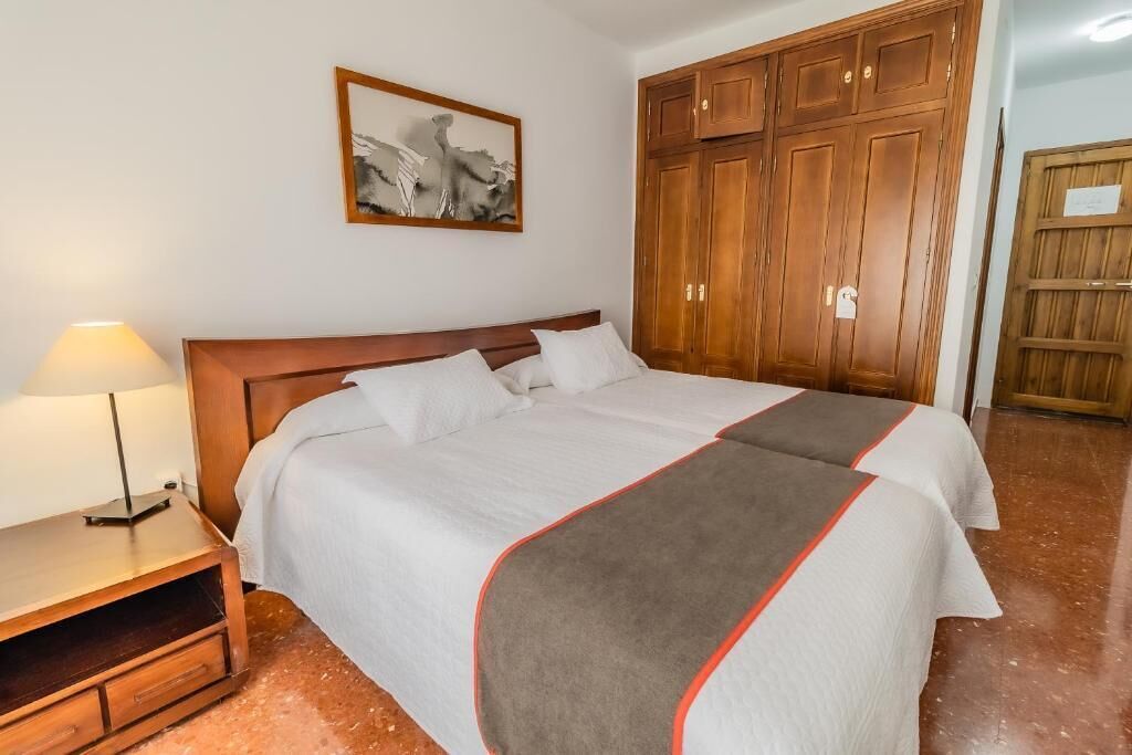 Una habitación de hotel con cama, mesita de noche, lámpara, armario y un cuadro en la pared.
