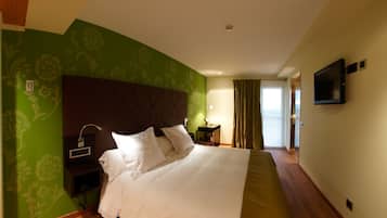 Hotelkamer met een groot bed, nachtkastje, een aan de muur bevestigde televisie en een raam met gordijnen.