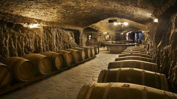 A dimly lit underground wine cellar with stone walls and wooden barrels arranged in rows.