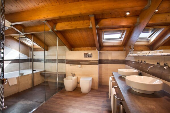 A modern bathroom with a skylight, a bathtub, two toilets, and a large vanity with two sinks.