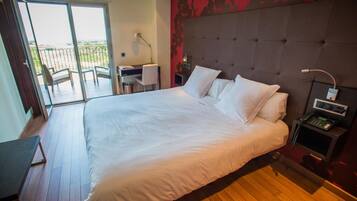 Habitación de hotel con una cama grande, un escritorio, una silla y vistas al exterior a través de una puerta corrediza.