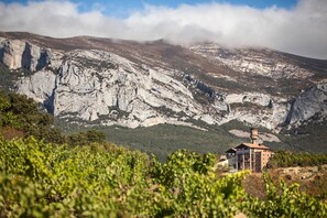 A building with a tower on a hillside, surrounded by rocky terrain and greenery.