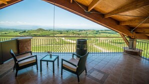 Ein Balkon mit Blick auf einen Weinberg, einer Holzbalkendecke und einem Barhocker.