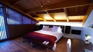 Ein modernes Schlafzimmer mit einem großen Bett, Holzbalkendecke, einer Sitzbank, einem Schreibtisch und einem Blumentopf.