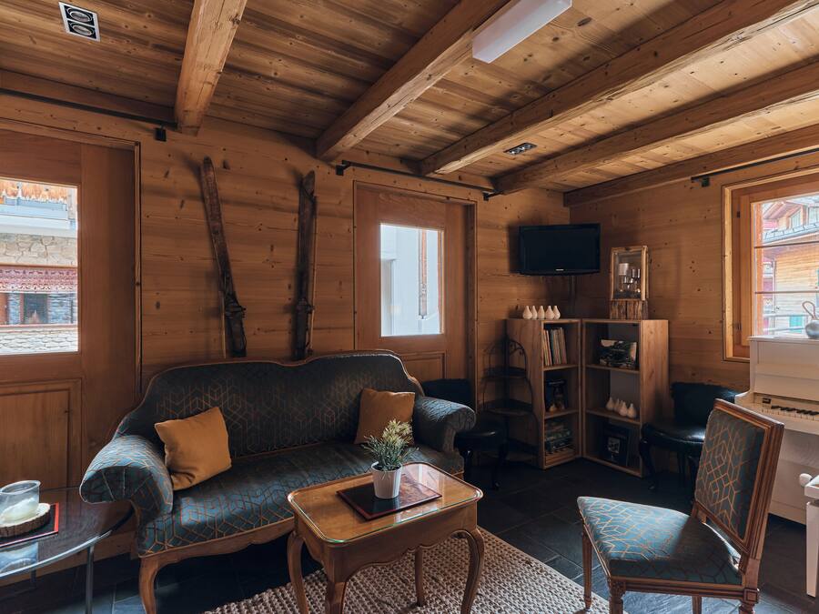Un interior de cabaña acogedor con techo de madera, un sofá, una silla, un piano y un televisor.