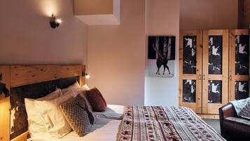 Ein Schlafzimmer mit Holz-Kopfteil, einem Bett mit gemusterten Bettbezügen, einer Wandleuchte und einem Holzschrank mit Glastüren.