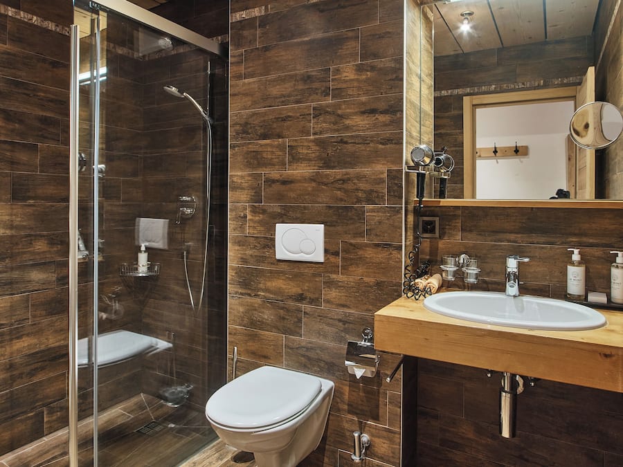 A modern bathroom with a wooden ceiling, a glass shower enclosure, a white toilet, and a wooden vanity with a mirror.