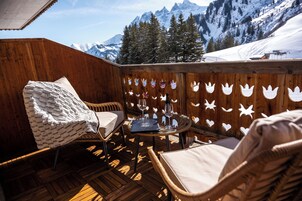 Una terraza de madera con muebles de mimbre, una mesa con vasos y vistas a montañas nevadas.