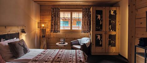 Una habitación acogedora con cama, una silla, una mesita con lámpara y una ventana con cortinas.