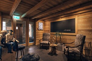 Interior de madera con pared de piedra, una obra de arte enmarcada y una zona de estar con sillas y una mesa.