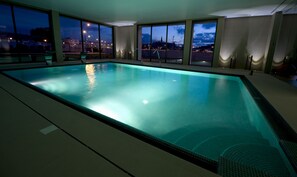 Une grande piscine intérieure offrant une vue sur le paysage urbain au crépuscule.