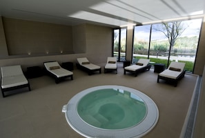 A spa area with a hot tub surrounded by lounge chairs, large windows, and a view of a lake. - Villa Batalha (Batalha)