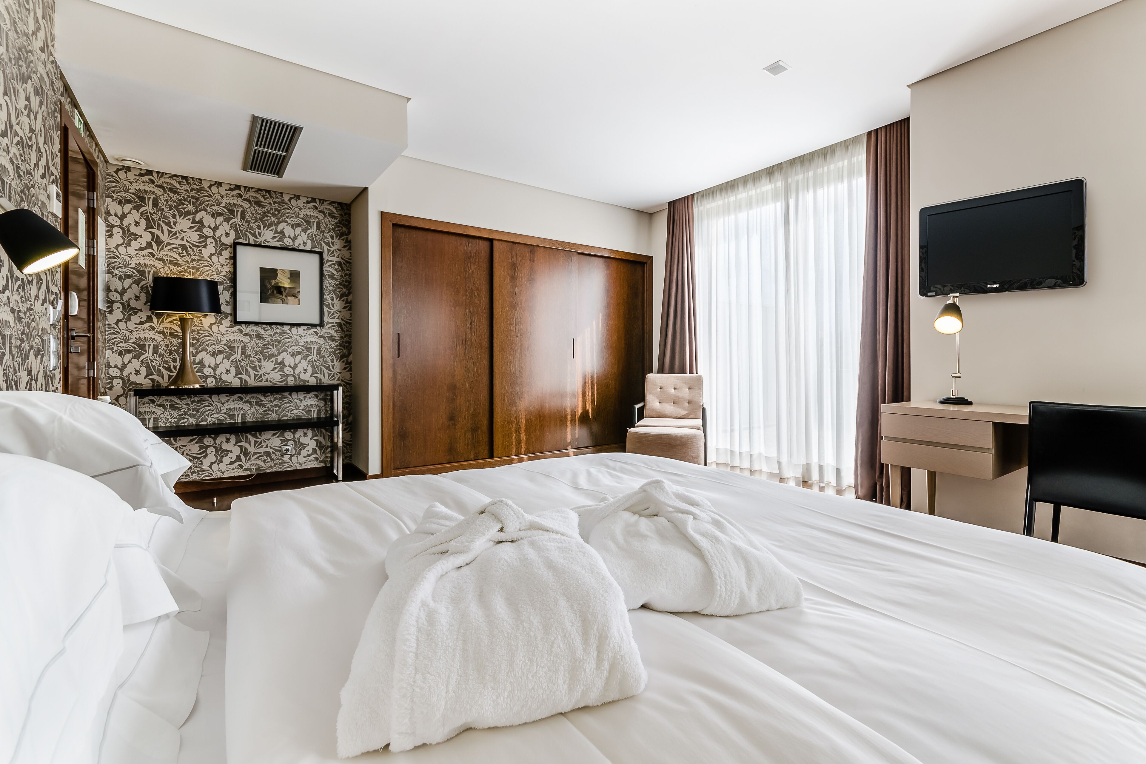 Una habitación de hotel con una cama grande, un escritorio, una silla, un televisor y un armario.