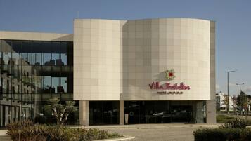 Un hotel moderno con fachada curva, ventanas amplias y un logo con una flor y estrellas.