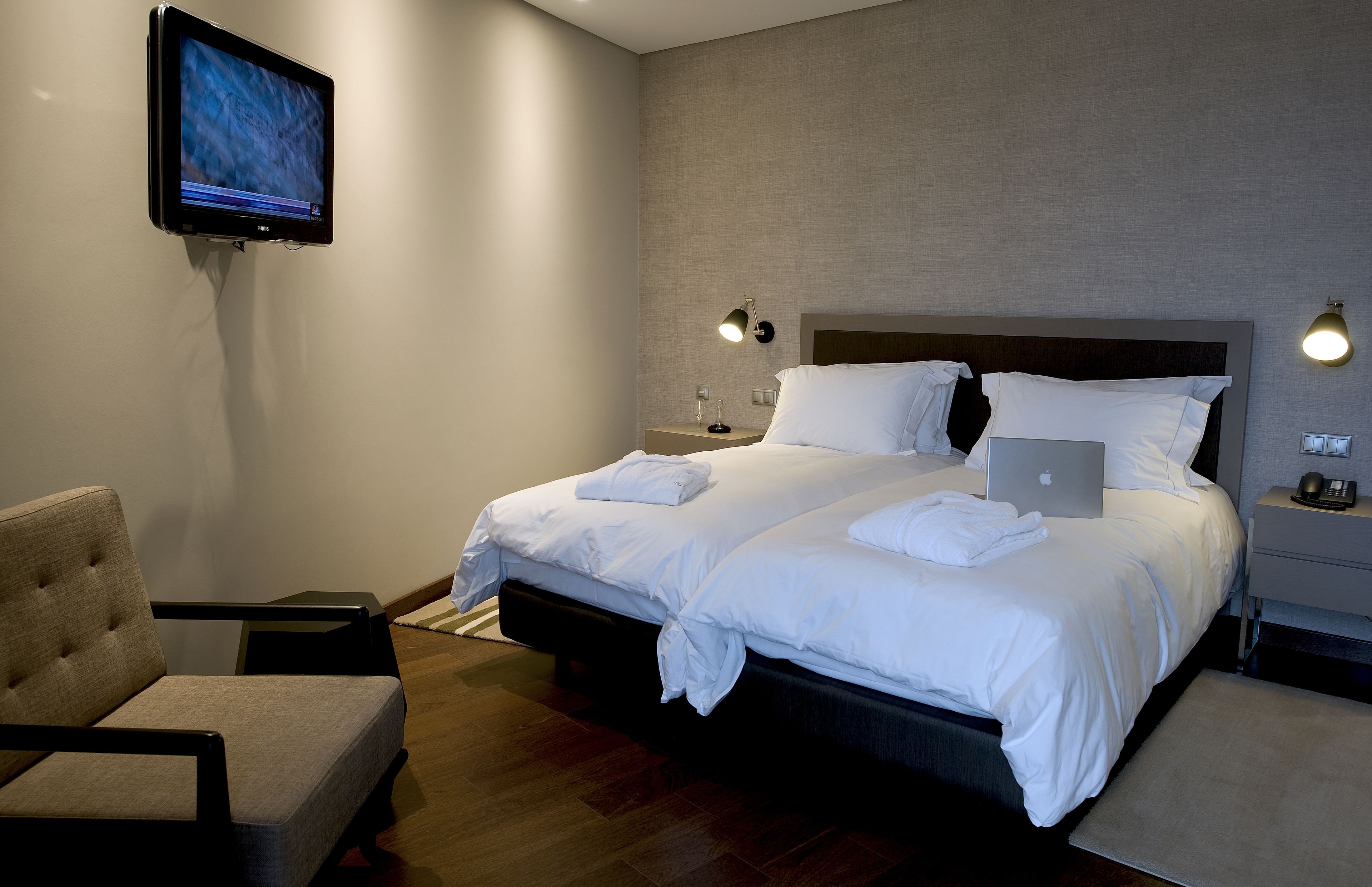 A modern hotel room with a large bed, a chair, a desk, and a flat-screen TV mounted on the wall.