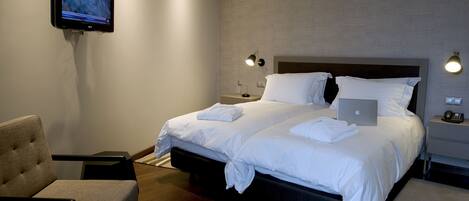 A modern hotel room with a large bed, a chair, a desk, and a flat-screen TV mounted on the wall.