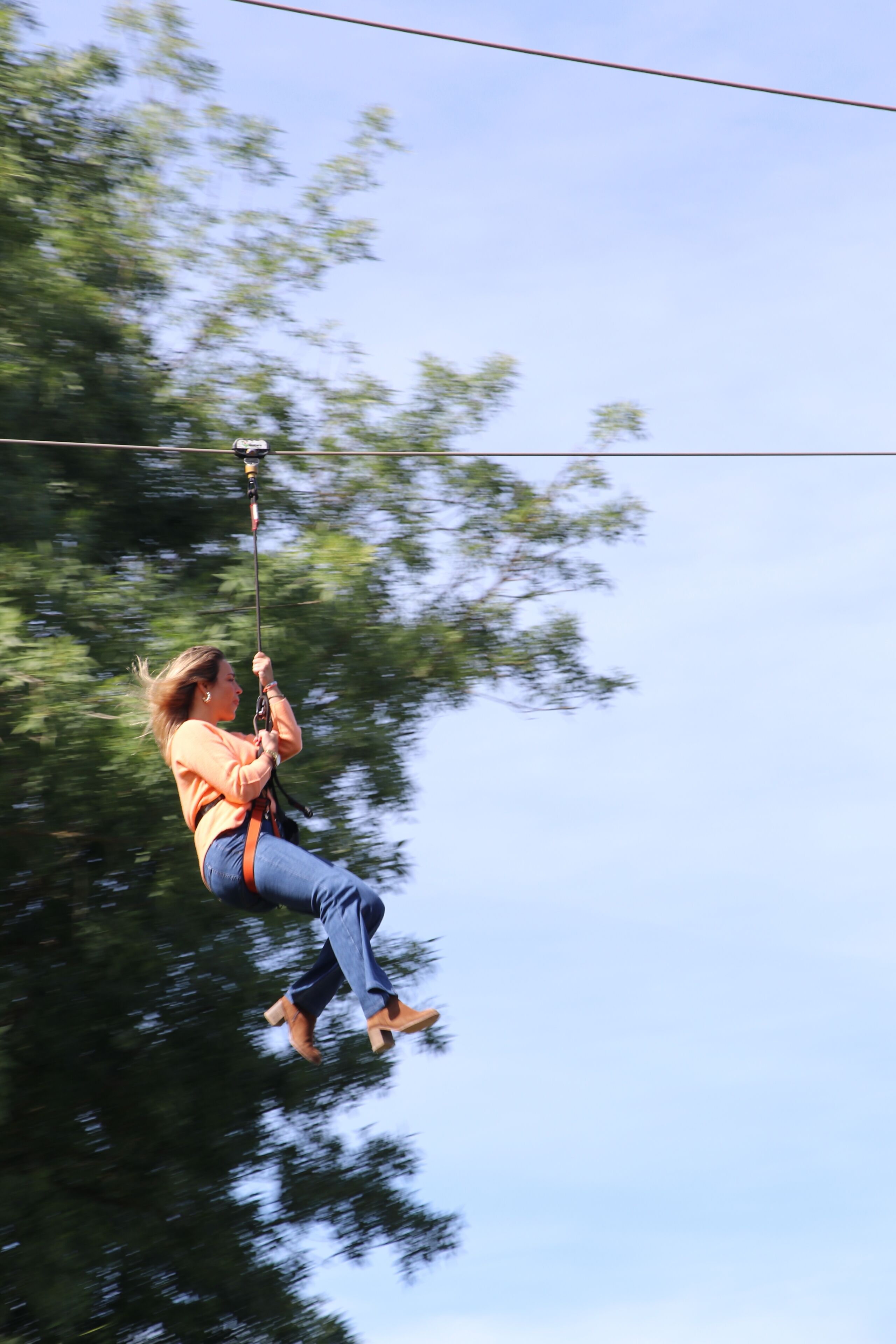 A person suspended in mid-air, holding onto a harness, with a clear sky and trees in the background.