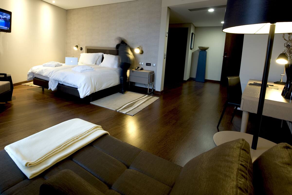 A modern hotel room with a large bed, a desk, a chair, and a television mounted on the wall.