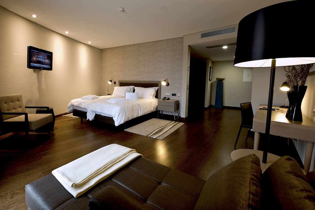 A hotel room with a bed, a desk, a chair, a TV, and a lamp.