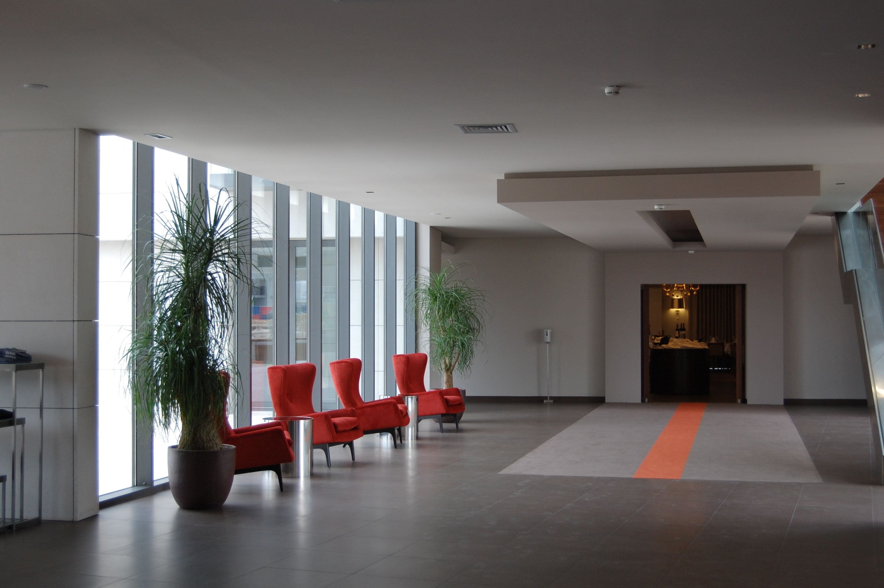Un hall d’entrée moderne avec de grandes fenêtres, des fauteuils rouges et des plantes en pot.