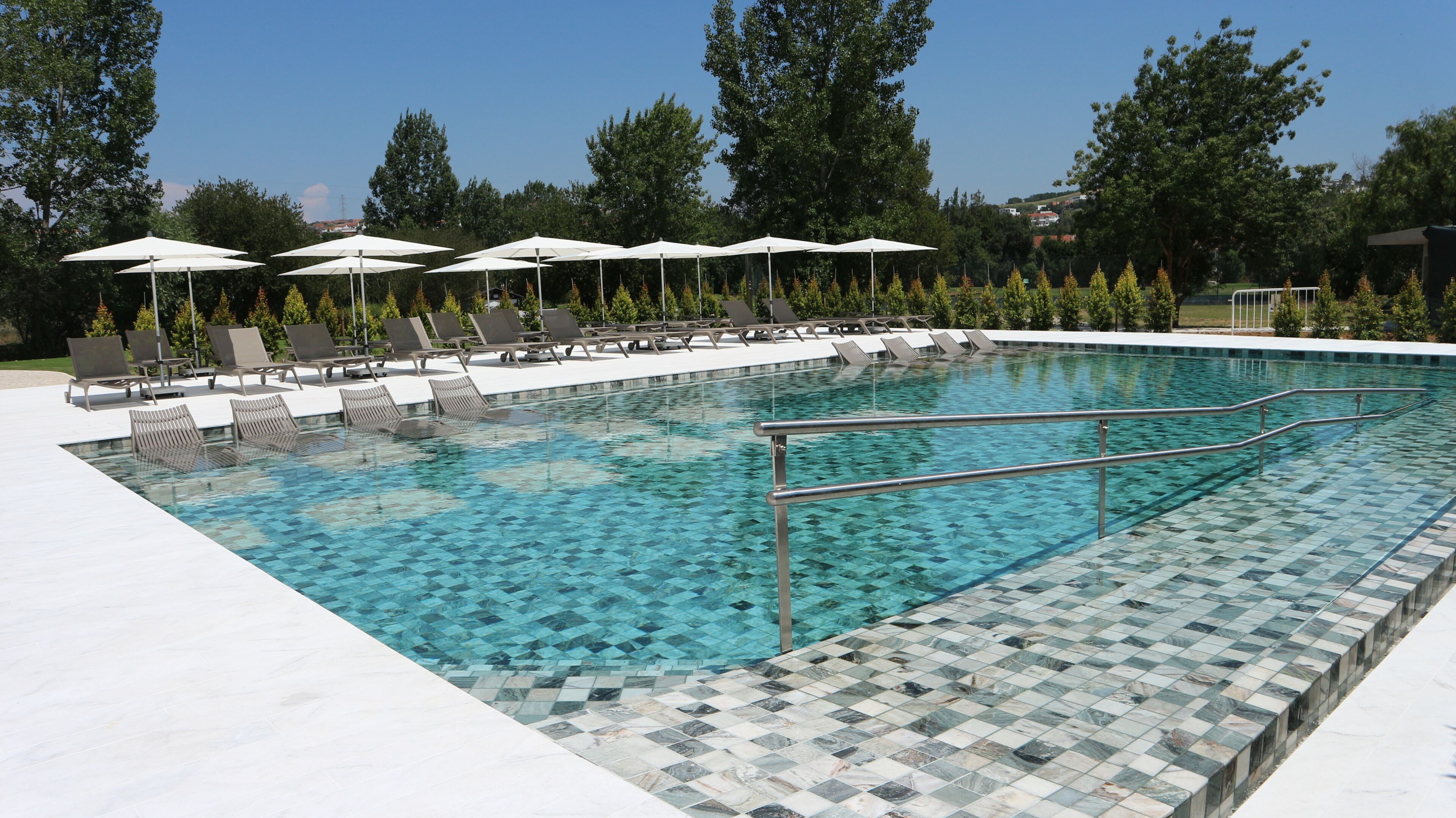 A swimming pool with tiled edges, sun loungers, and umbrellas.