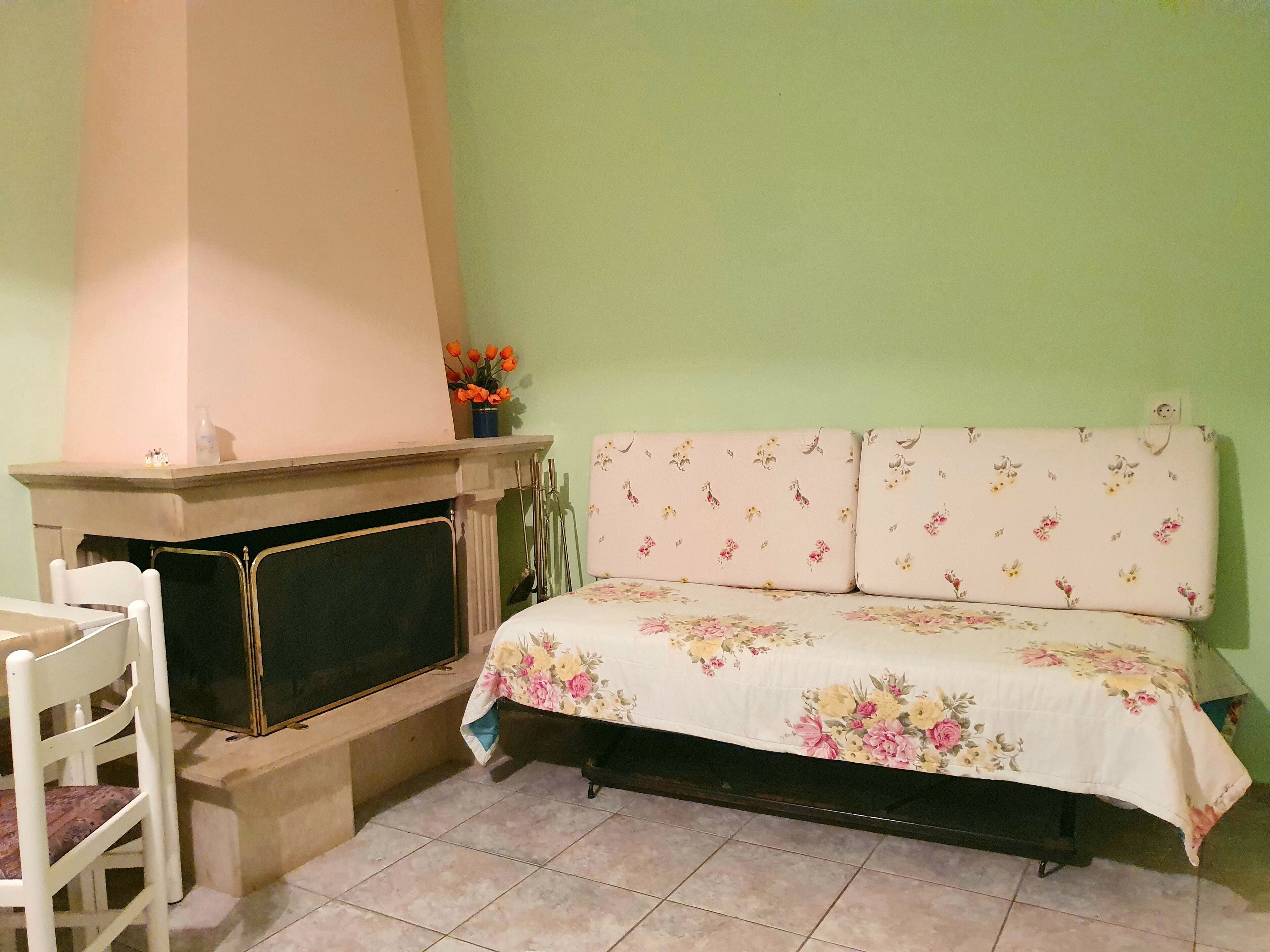 A room with a fireplace, a bed with floral bedding, a chair, and a small table with a vase of flowers.