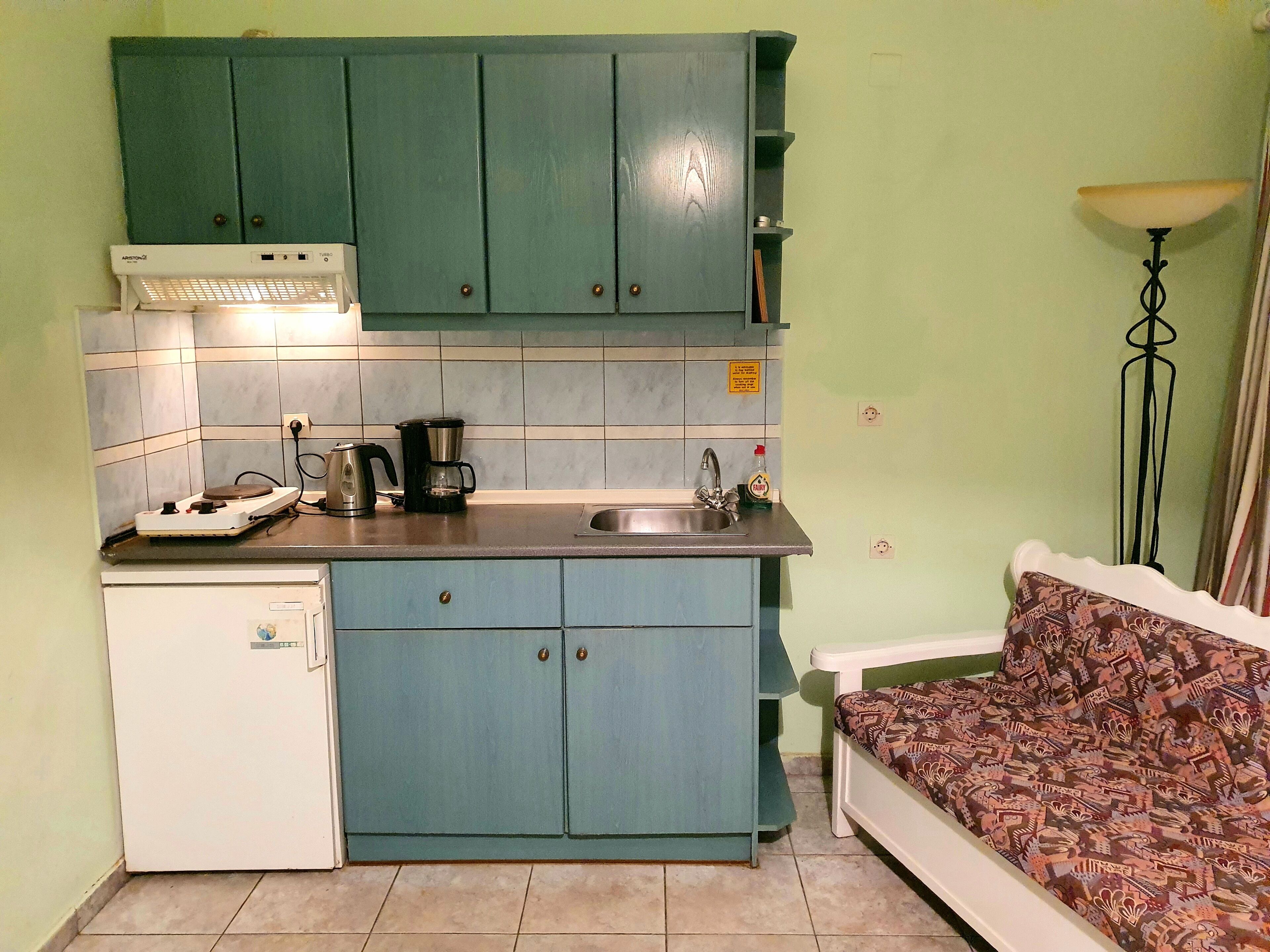 Une cuisine de taille réduite avec des meubles de couleur turquoise, un réfrigérateur blanc, une machine à café et un évier.