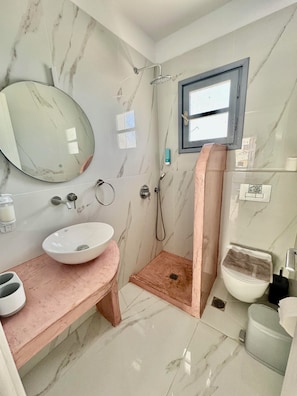 Une salle de bain avec un sol en marbre, un lavabo blanc, un miroir, une douche et des toilettes.