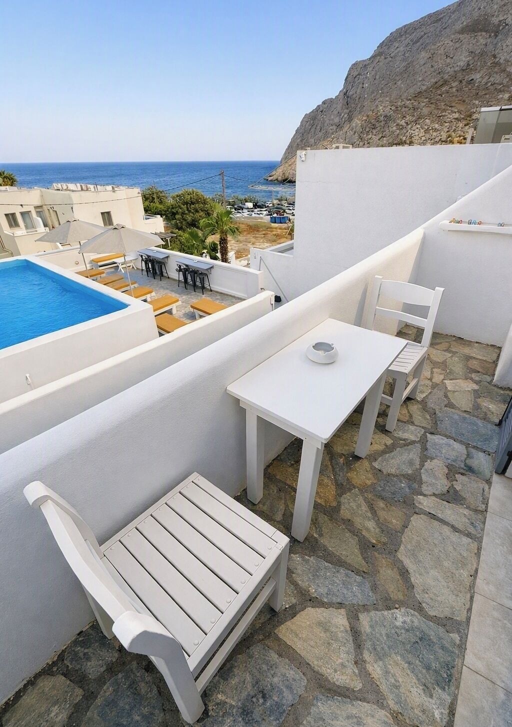 A rooftop terrace with a pool, white furniture, and a view of the sea.