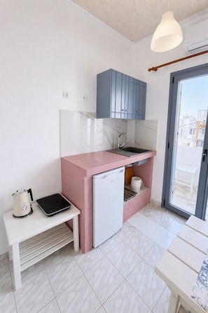 A compact kitchen with a built-in dishwasher, a small countertop, and a window overlooking a residential area. - Zacharakis Studios (Santorini)