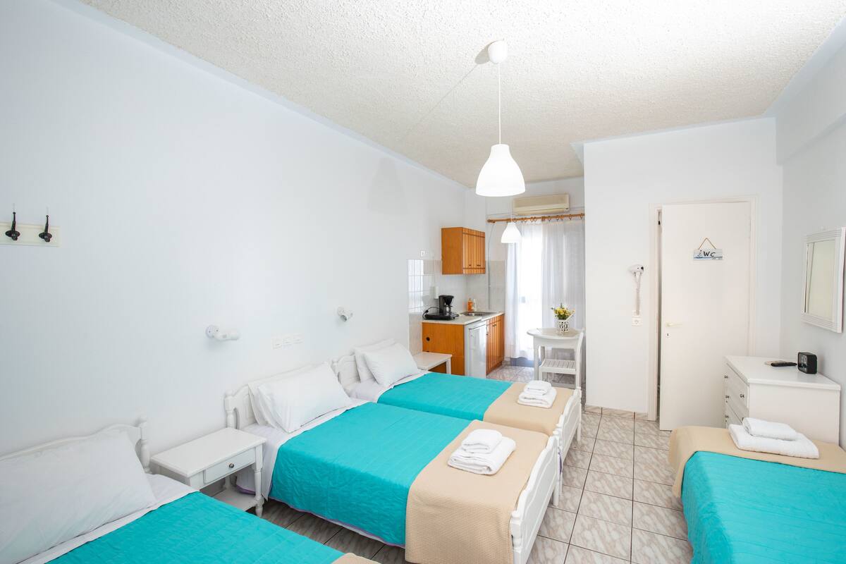 A hotel room with two beds, a desk, a small kitchenette, and a bathroom.