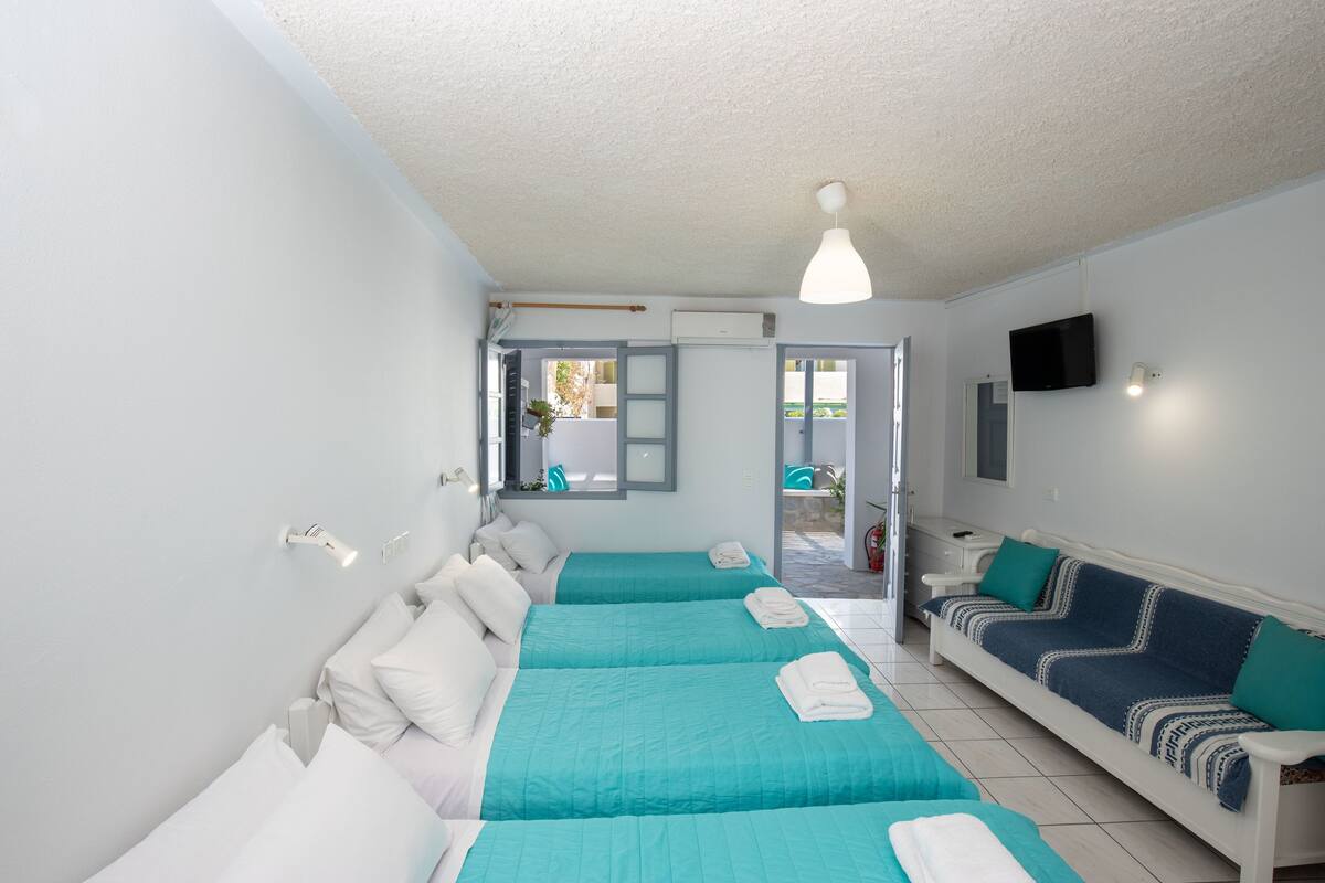 A room with two beds, a sofa, a TV, and a window.
