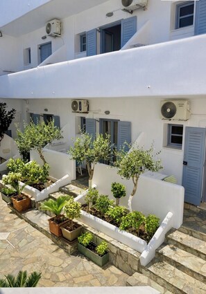 A white building with blue shutters, air conditioning units, and potted plants arranged along the steps.