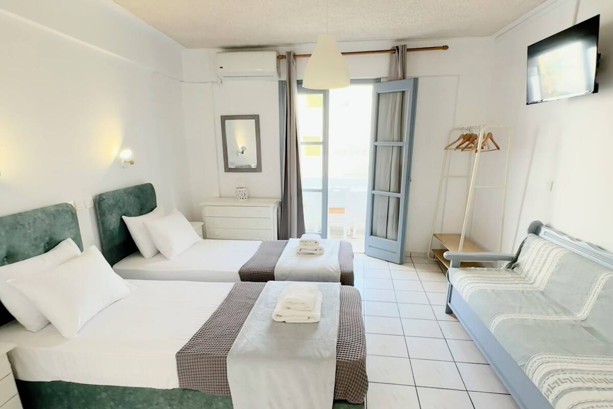 A hotel room with two beds, a TV, a wardrobe, and a balcony.
