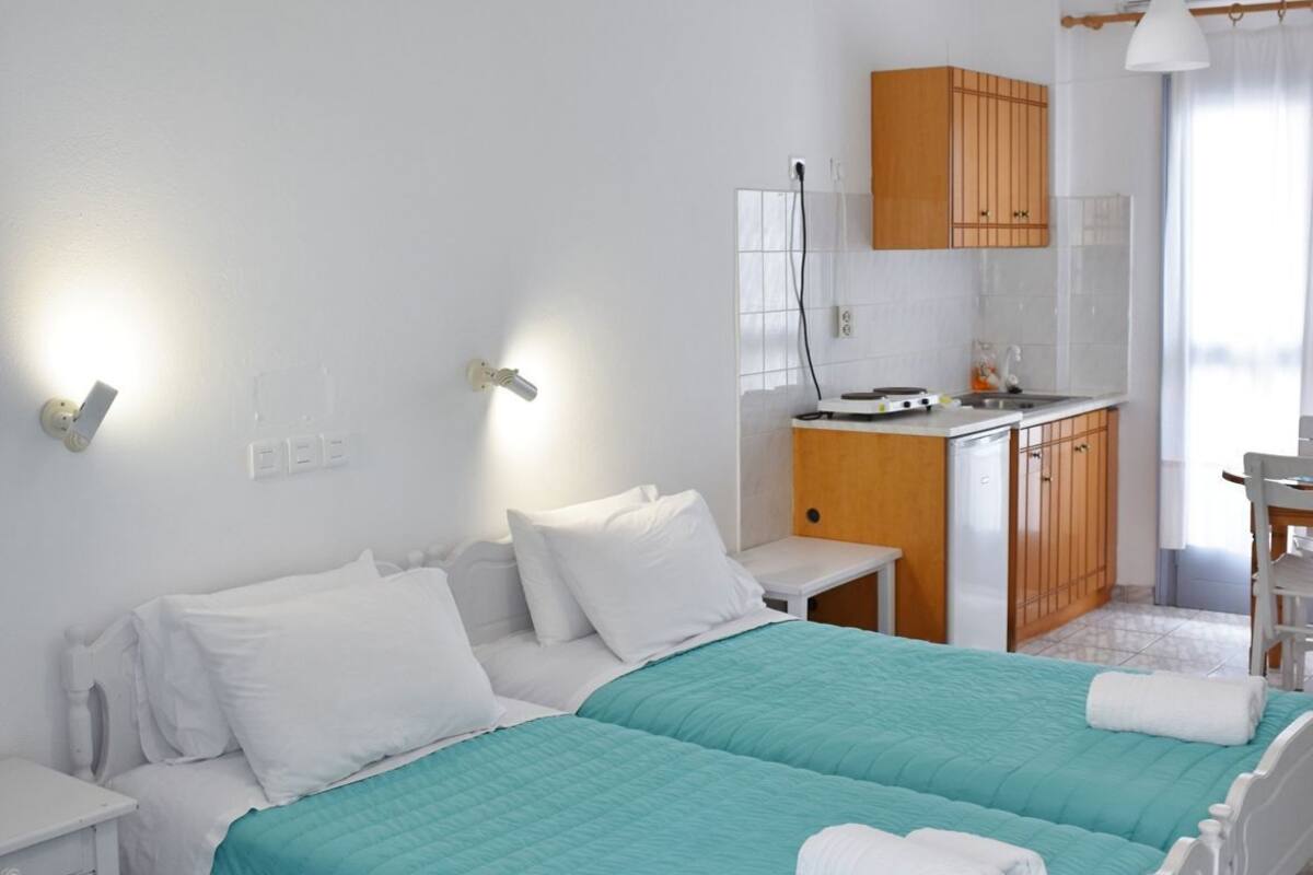 A hotel room with two beds, a kitchenette, a small table, and a window with curtains.