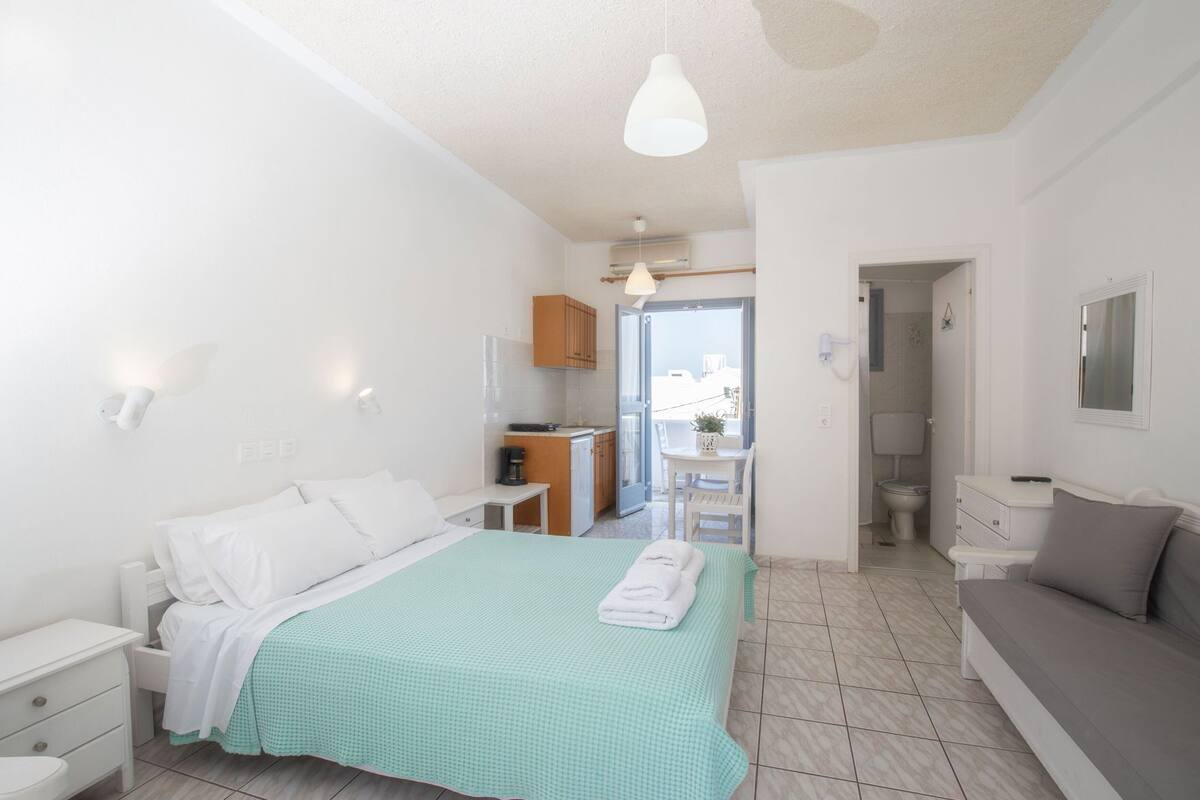 A hotel room with a bed, a sofa, a small table, a kitchenette, and a bathroom.