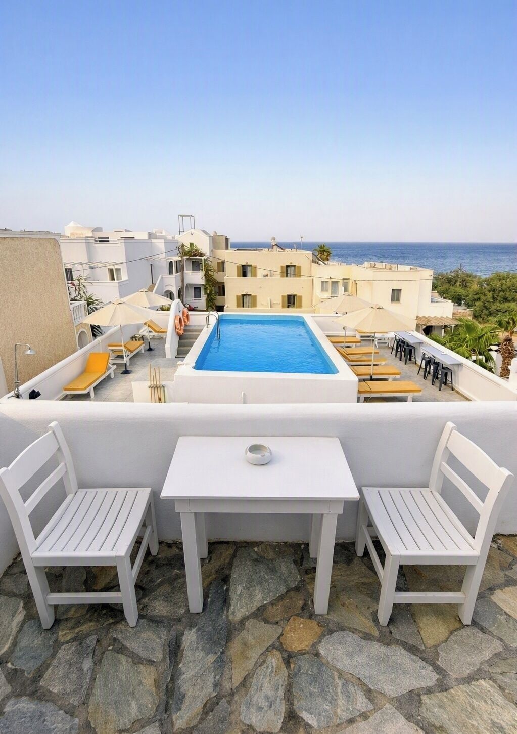 A rooftop terrace with a swimming pool, white furniture, and a view of the sea.