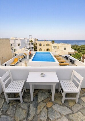 A rooftop terrace with a swimming pool, white furniture, and a view of the sea. - Zacharakis Studios (Santorini)