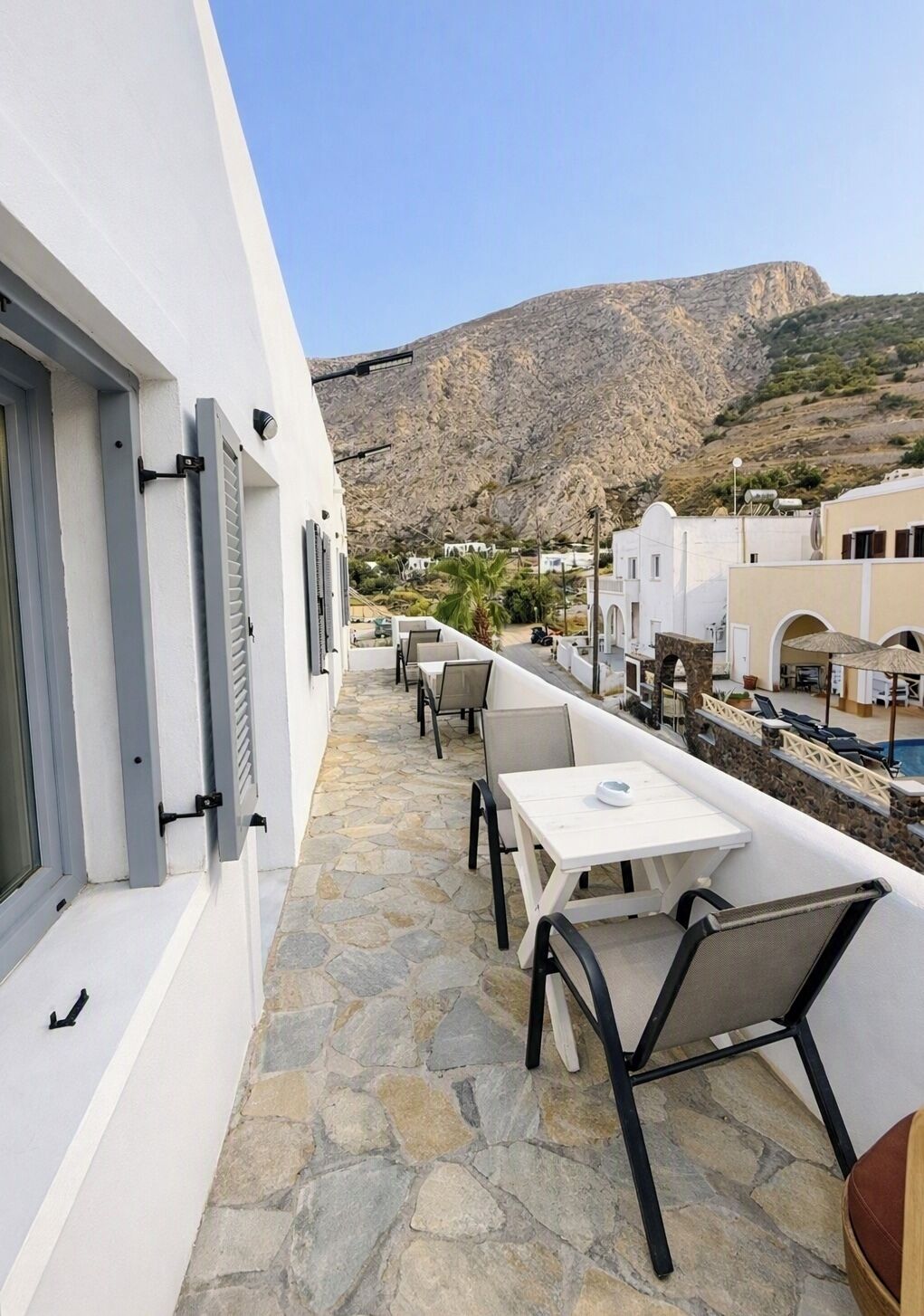 A balcony with stone flooring, white furniture, and a view of a mountainous landscape.