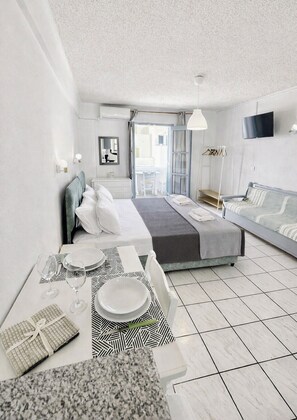 A modern hotel room with a bed, a sofa, a dining table with plates and glasses, and a television on the wall.