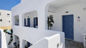 A white building with a blue door, stone steps, and a small potted plant.