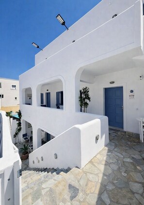 A white building with a blue door, stone steps, and a small potted plant. - Zacharakis Studios (Santorini)