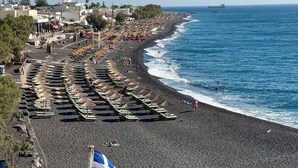 Una spiaggia con file di ombrelloni e lettini, una bandiera e una nave all'orizzonte.