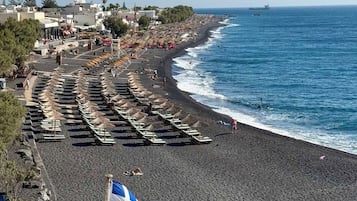 A beach with rows of umbrellas and lounge chairs, a flag, and a ship in the distance.