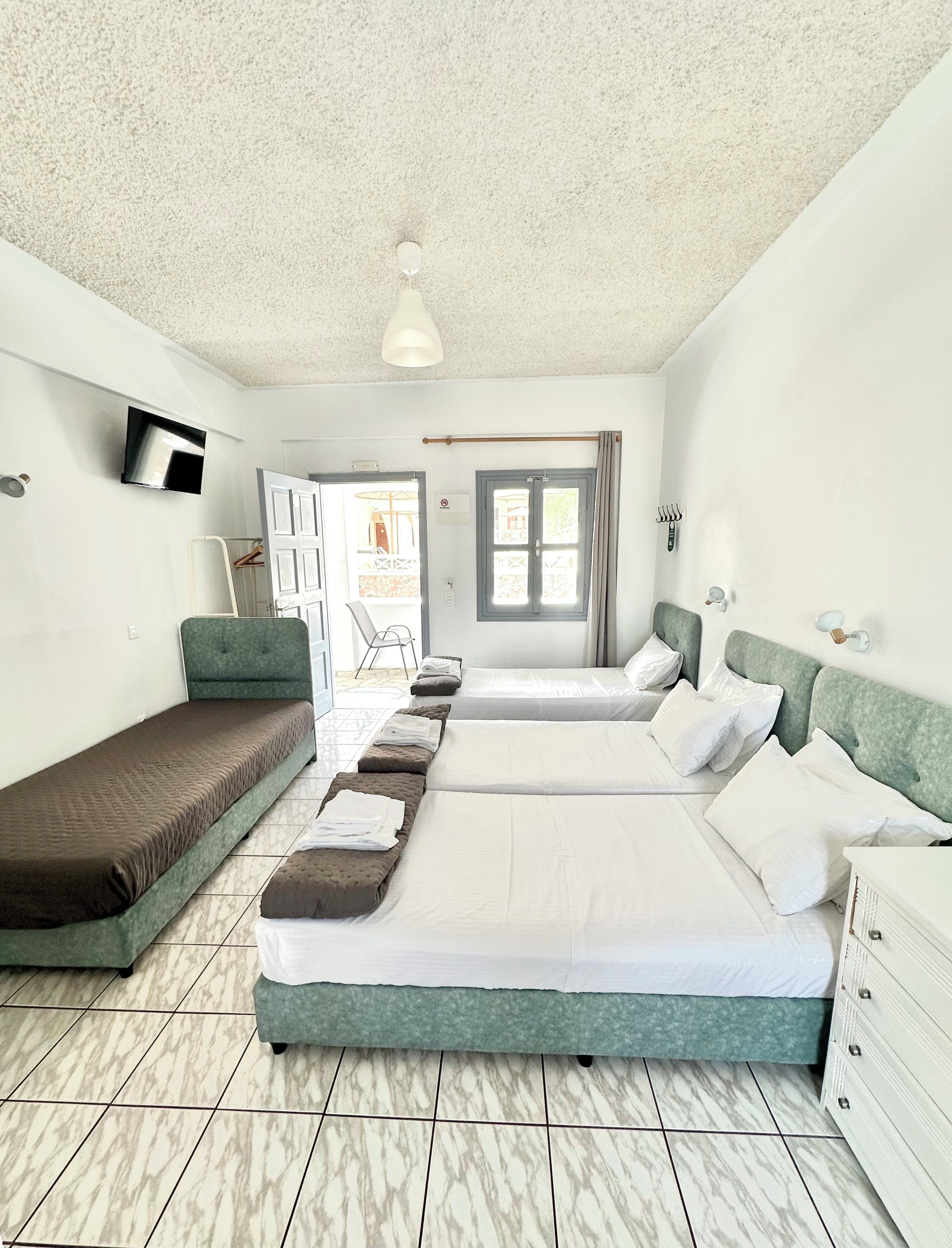 A hotel room with two beds, a television, a window, and a door leading to a balcony.