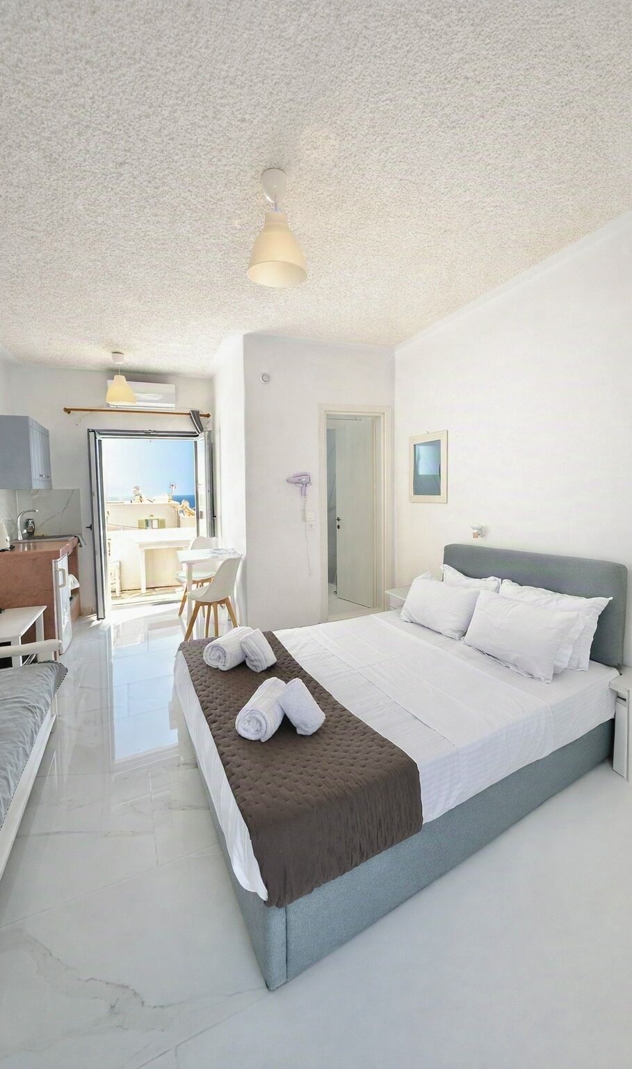 A hotel room with a bed, a desk, and a view of the sea.