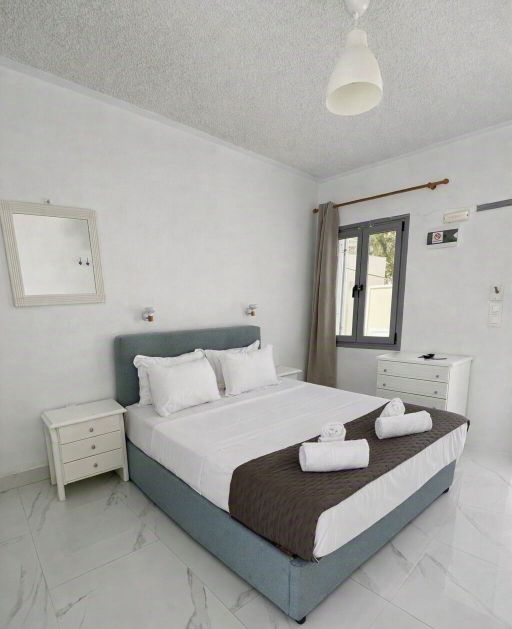 A bedroom with a bed, nightstands, a dresser, a window with curtains, and a ceiling light.
