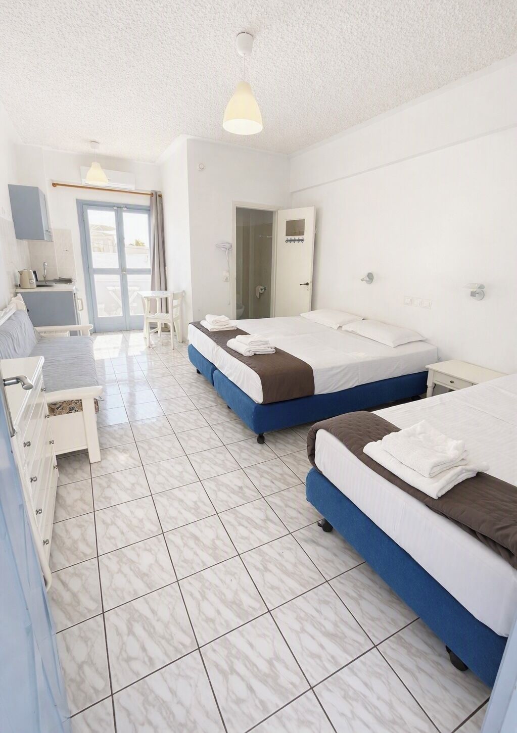Habitación de hotel con dos camas, kitchenette, baño y balcón.