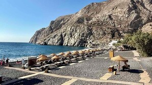 Una playa con tumbonas y sombrillas, un acantilado rocoso y un cielo azul despejado.