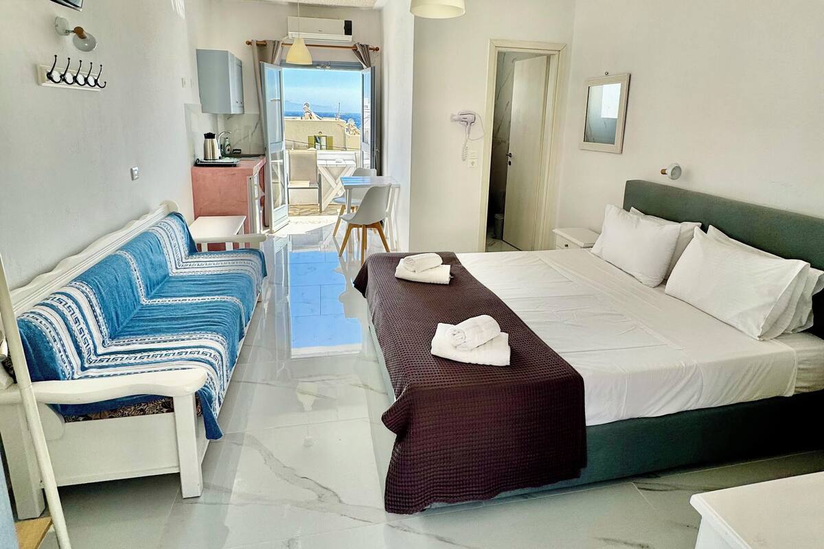 A hotel room with a bed, a sofa, a small table, and a view of the sea.